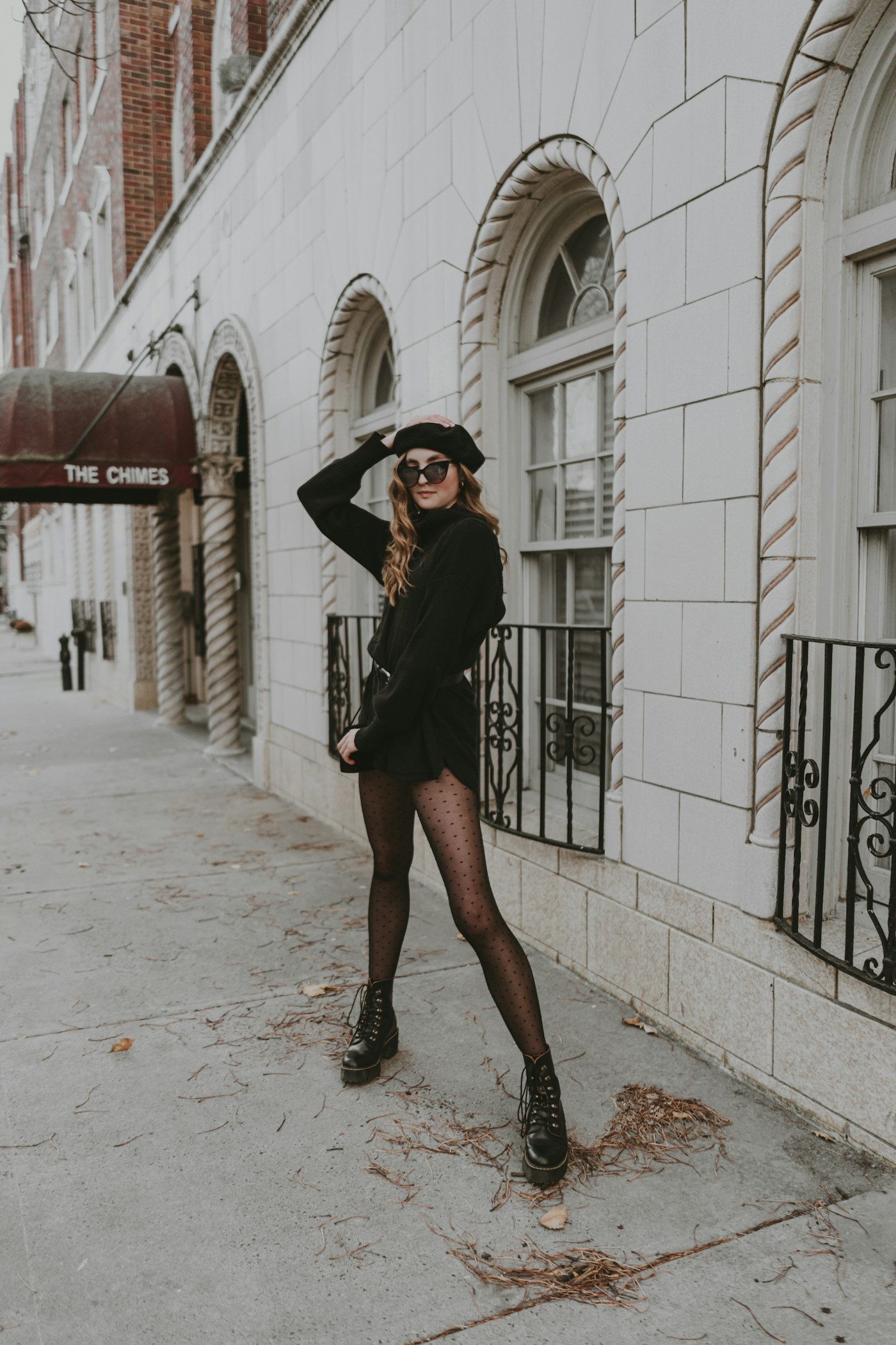 Woman wearing a black outfit and sunglasses beside a stone building