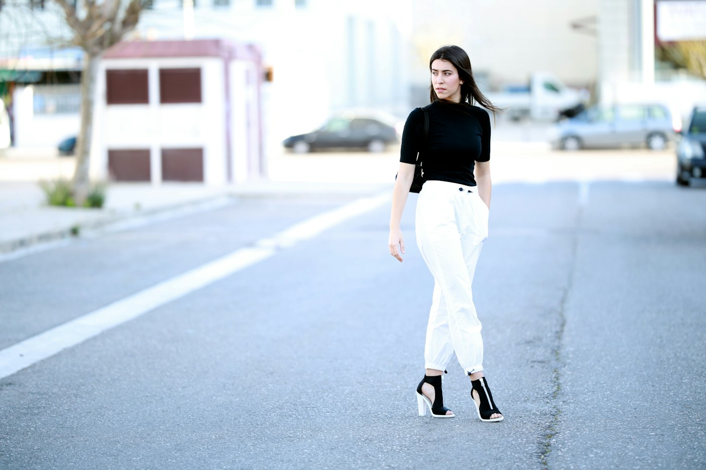 Woman wearing a black top and white trousers on a city street