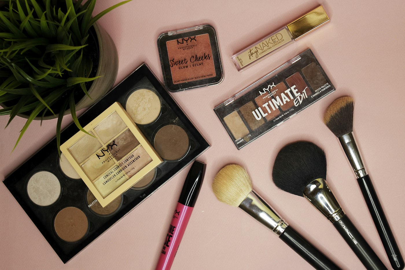 Cosmetics and makeup brushes arranged on a pale pink surface