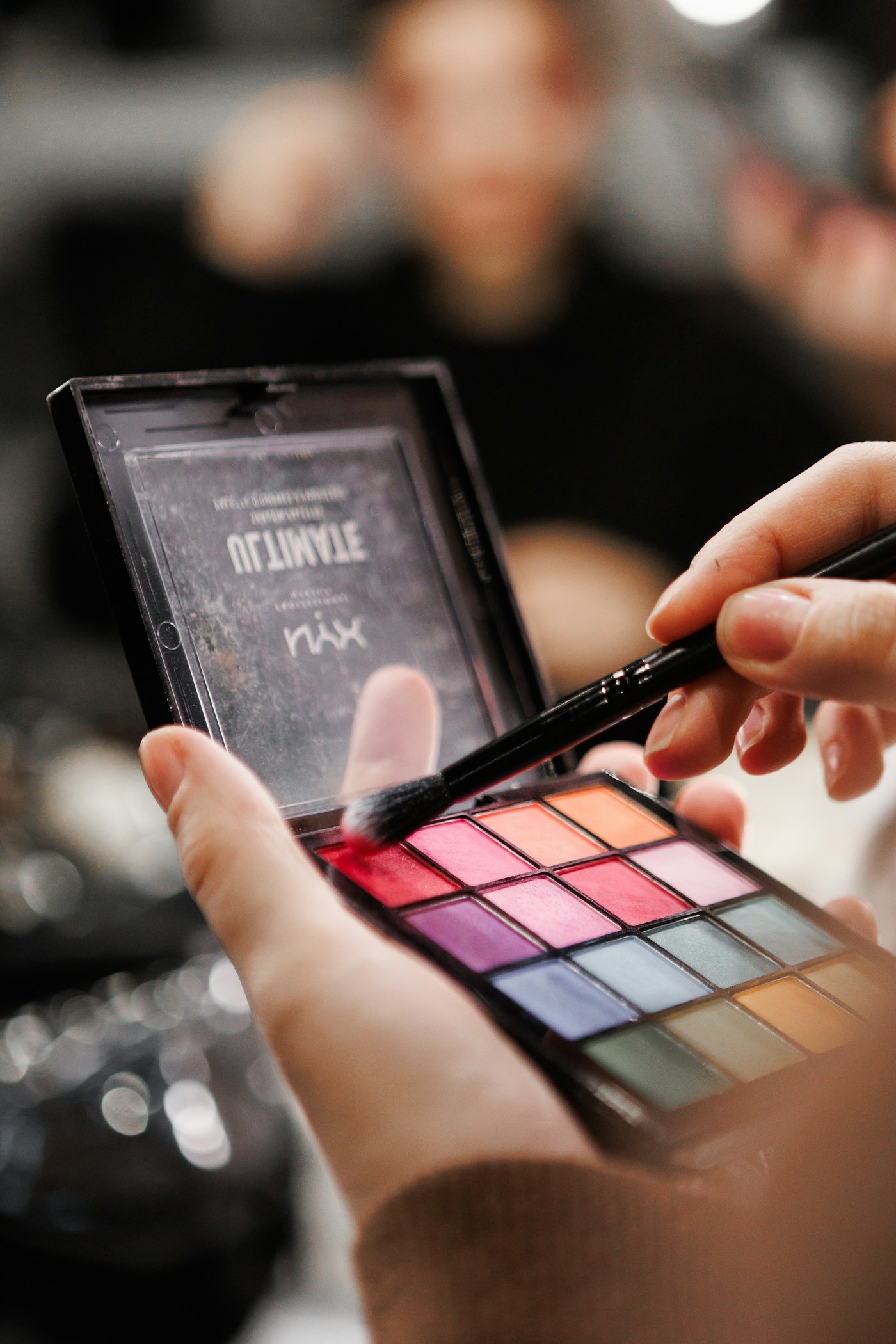Hands holding an eyeshadow palette and makeup brush