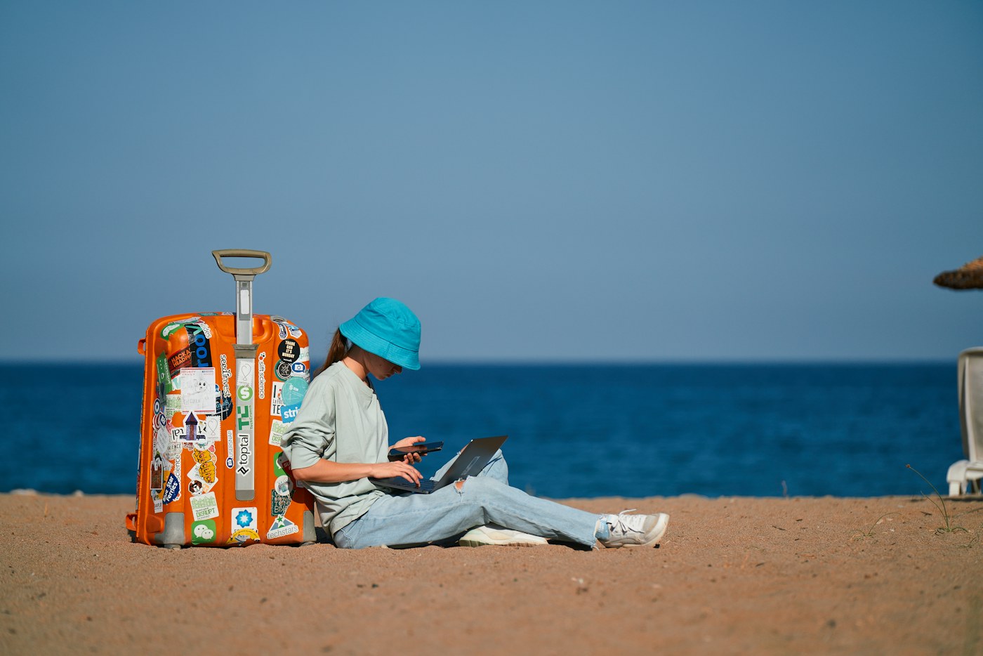 A traveler sitting on a beach beside a suitcase